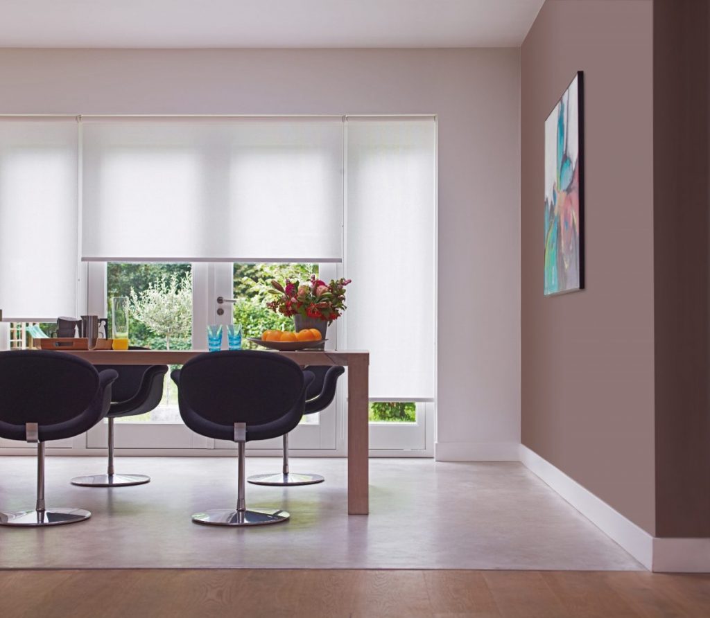 Lightly sheer interior roller blinds in a dining area or kitchen with garden view.